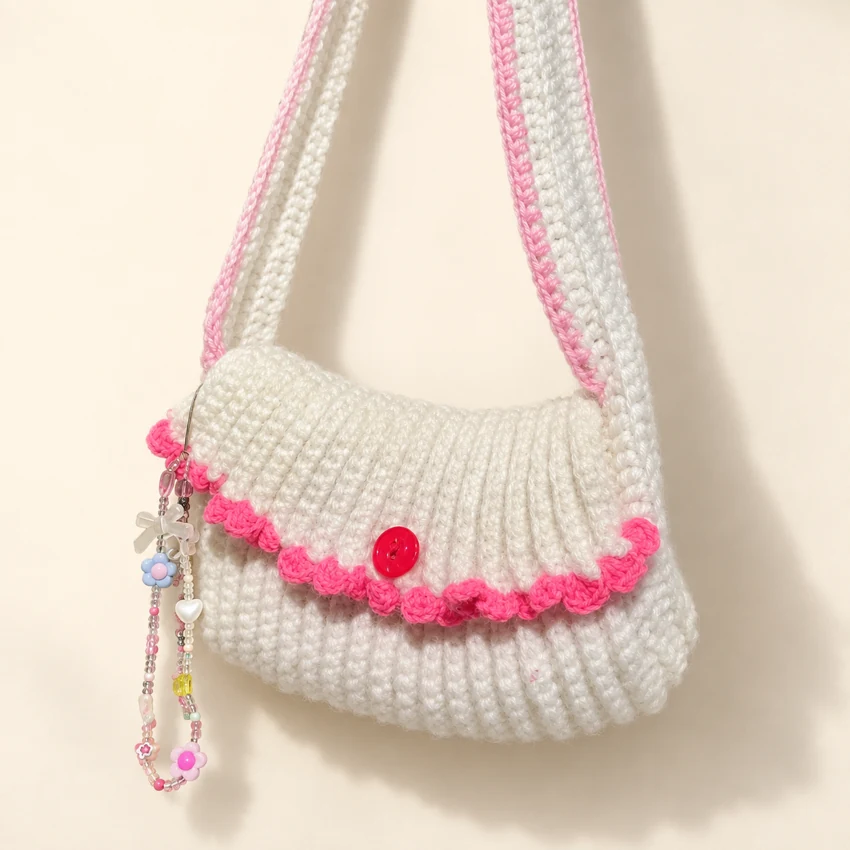 A white crochet shoulder bag with pink scalloped trim and a little charm