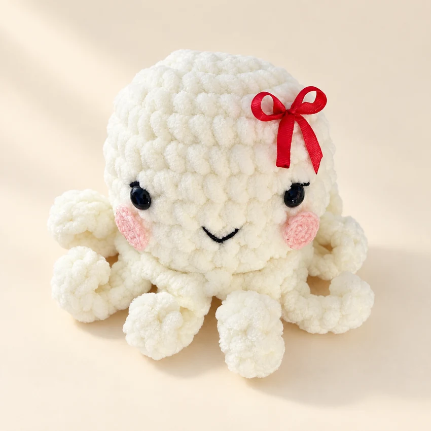 A smiling cream crochet octopus with a tiny red bow