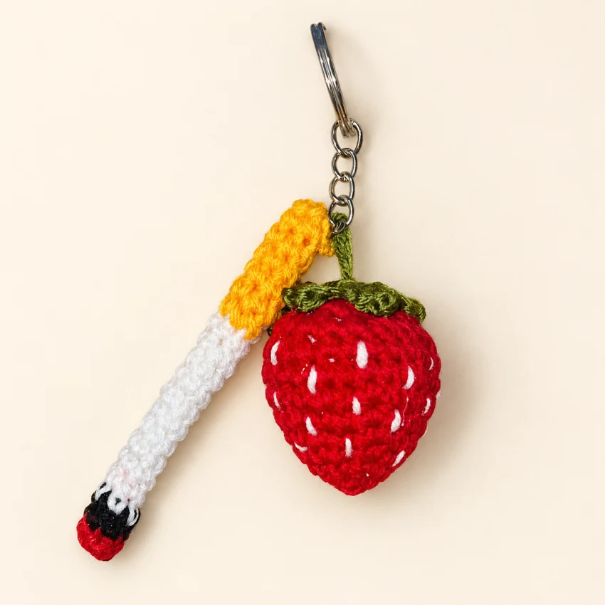 A red strawberry crochet keychain with a white and cigarette.