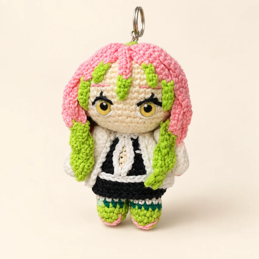 A small crocheted character with pink and green hair on a keychain