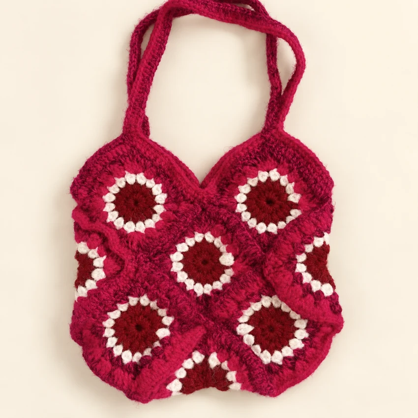 A fuchsia crochet sunburst bag with cream flower outlines