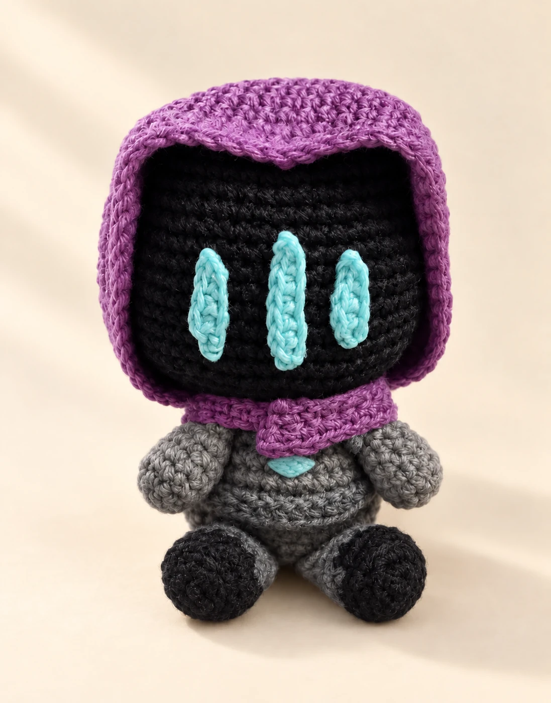 A purple-hooded Omen crochet character with turquoise face marks and a chest detail on a cream background