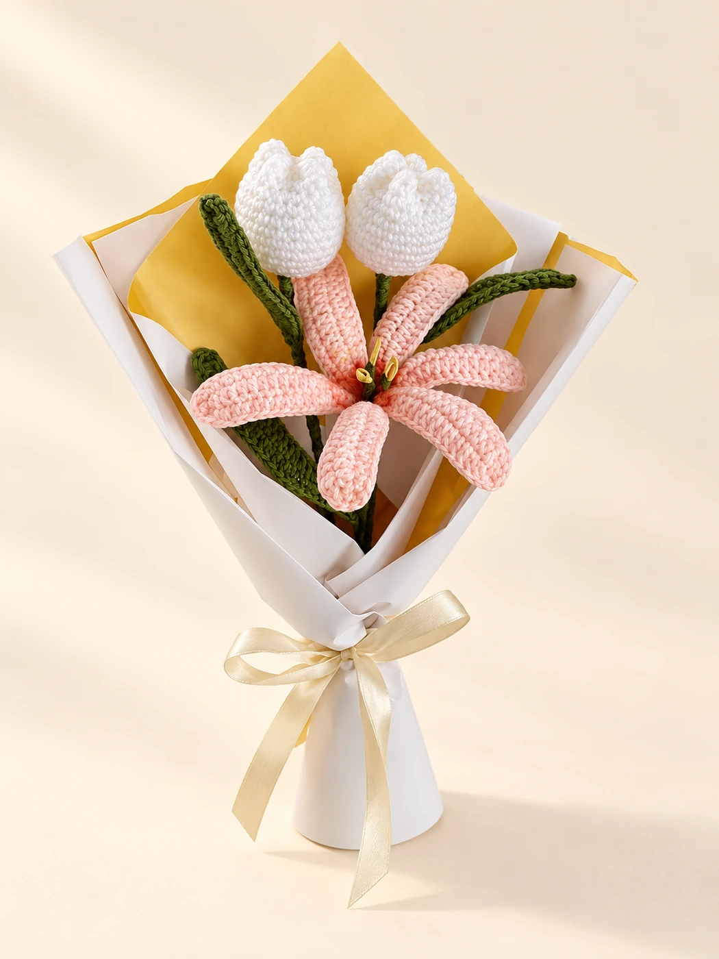 A pink and white crochet flower bouquet in paper wrapping with a cream ribbon on a cream background
