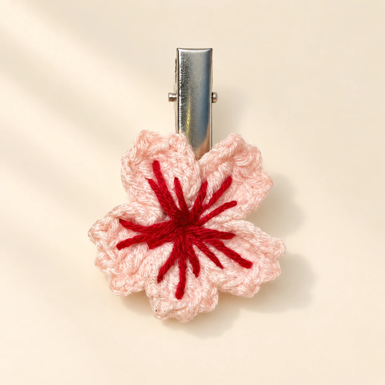 A blush crochet flower with a red embroidered center and silver hair clip for a cute look.