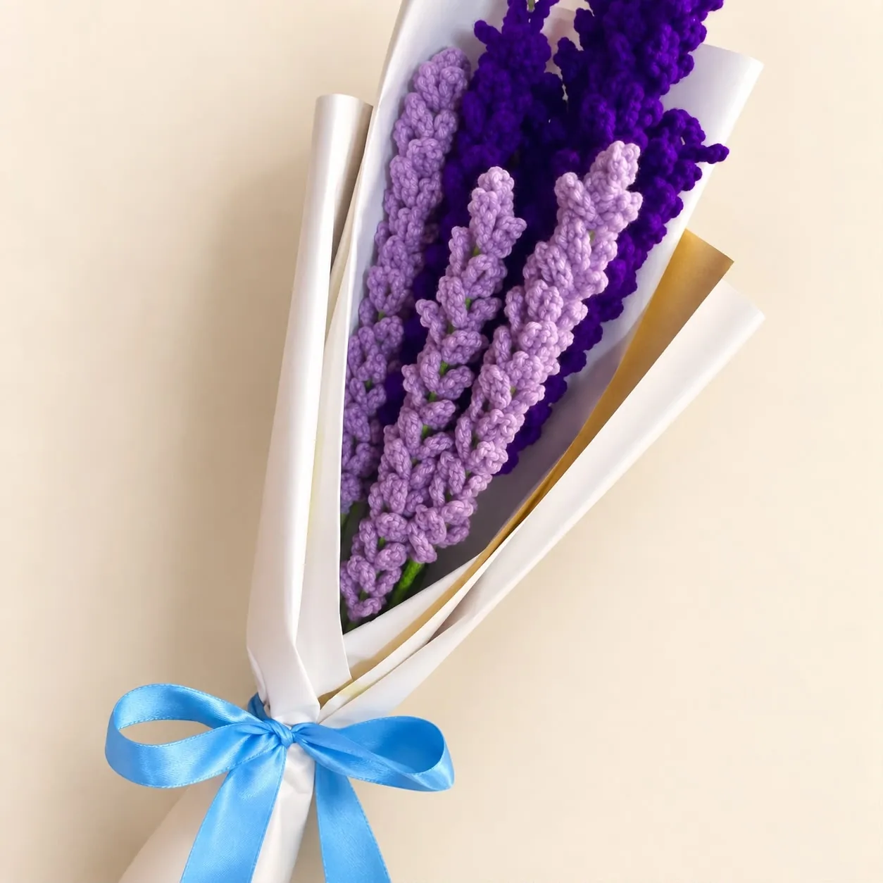 A bouquet of light and dark purple crochet lavender wrapped in white paper with a blue satin bow