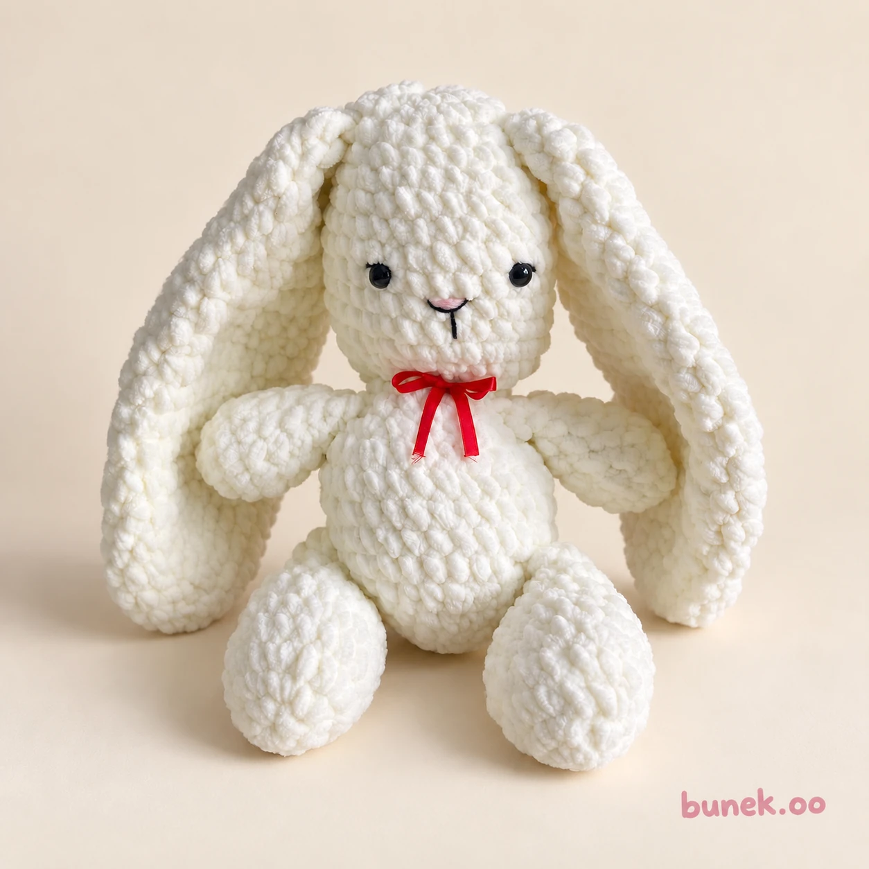 Cream crochet bunny with long floppy ears, black eyes and a red ribbon