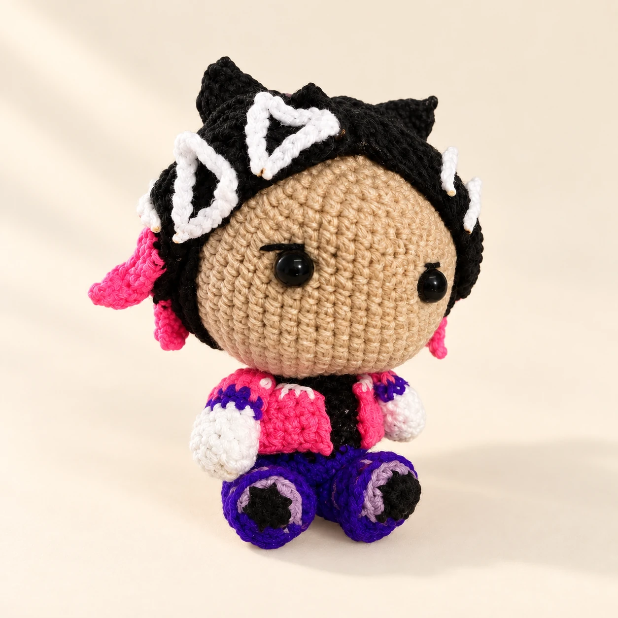 A Clove crochet doll with white hair decorations, a pink top and purple boots on a cream background