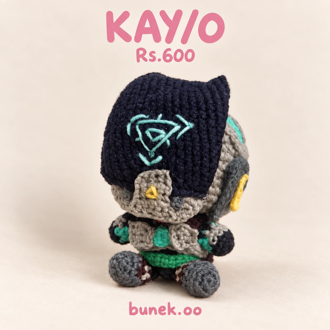KAY/O crochet robot doll with a dark face panel, turquoise emblem and gray body
