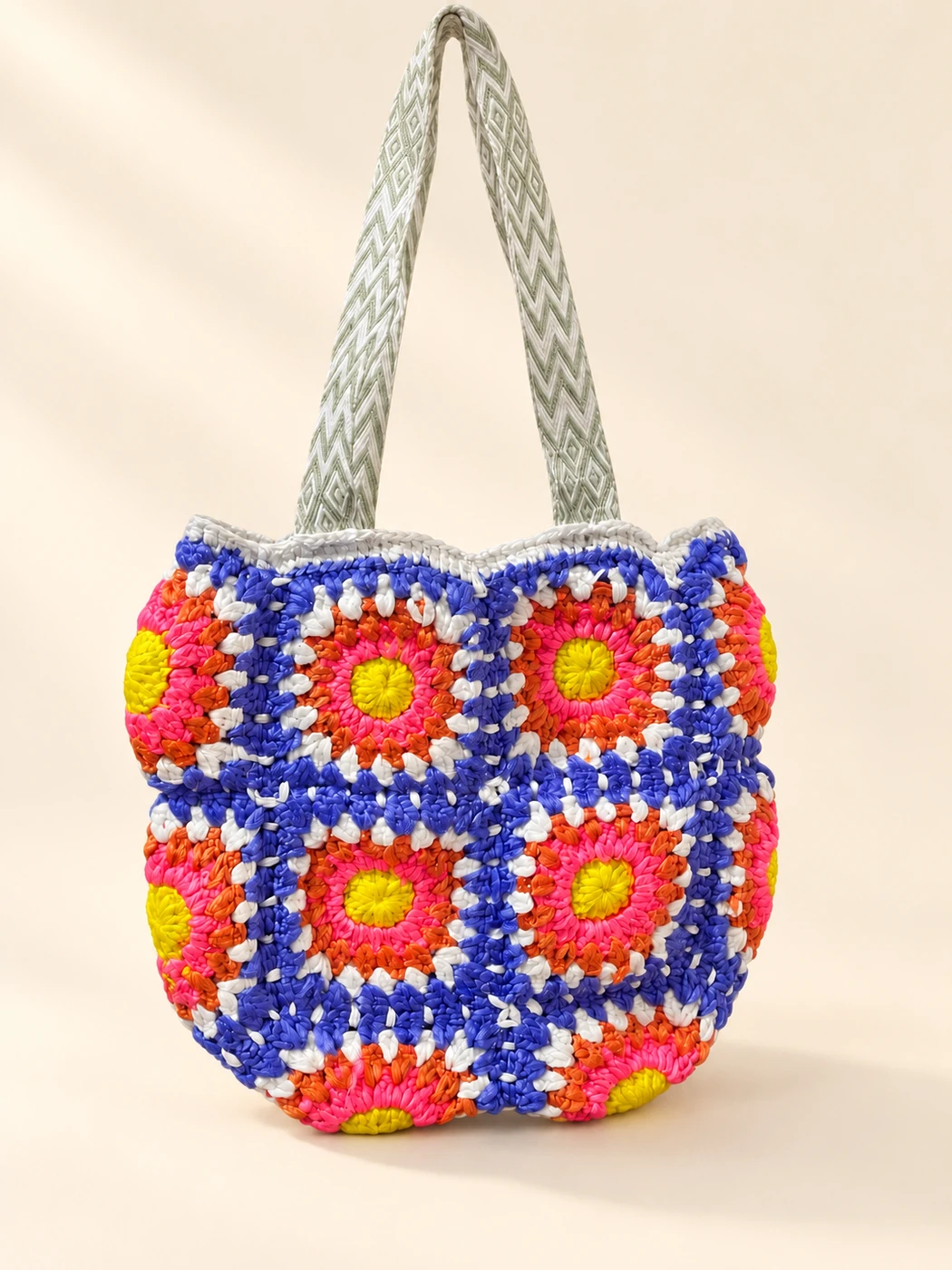 A multicolored floral granny-square crochet bag with cream patterned straps on a cream background