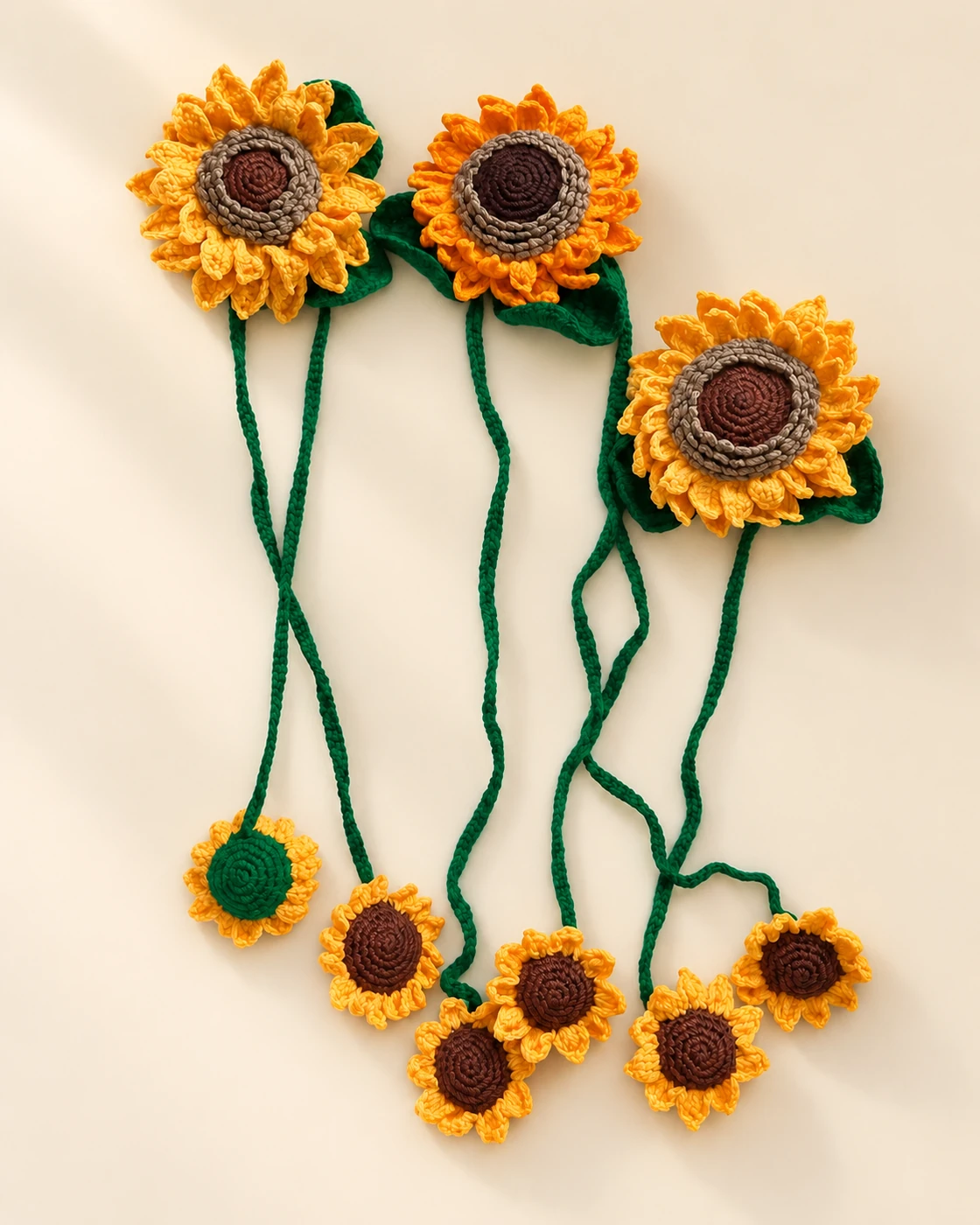 Three large crochet sunflowers with green cords and six small sunflower ends on a cream background
