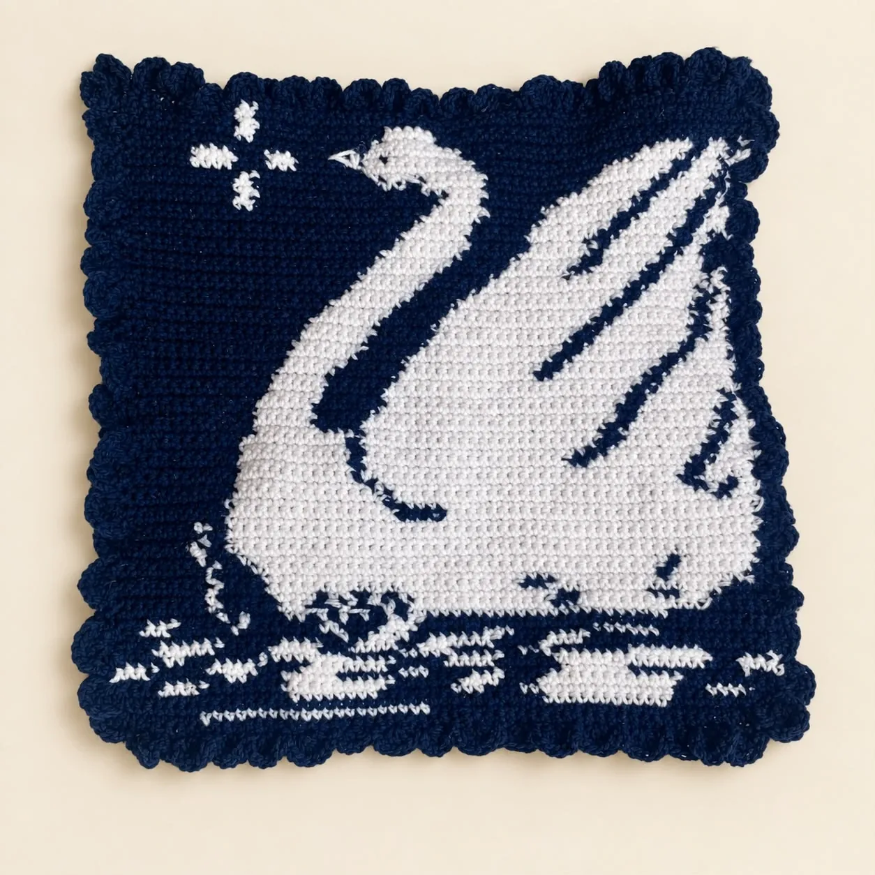 A square navy crochet tapestry with a white swan on stitched water and a scalloped border
